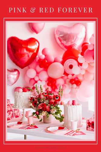 Pink and red Valentine's Day party with heart foil balloons, a balloon garland, florals, and heart-themed tableware.