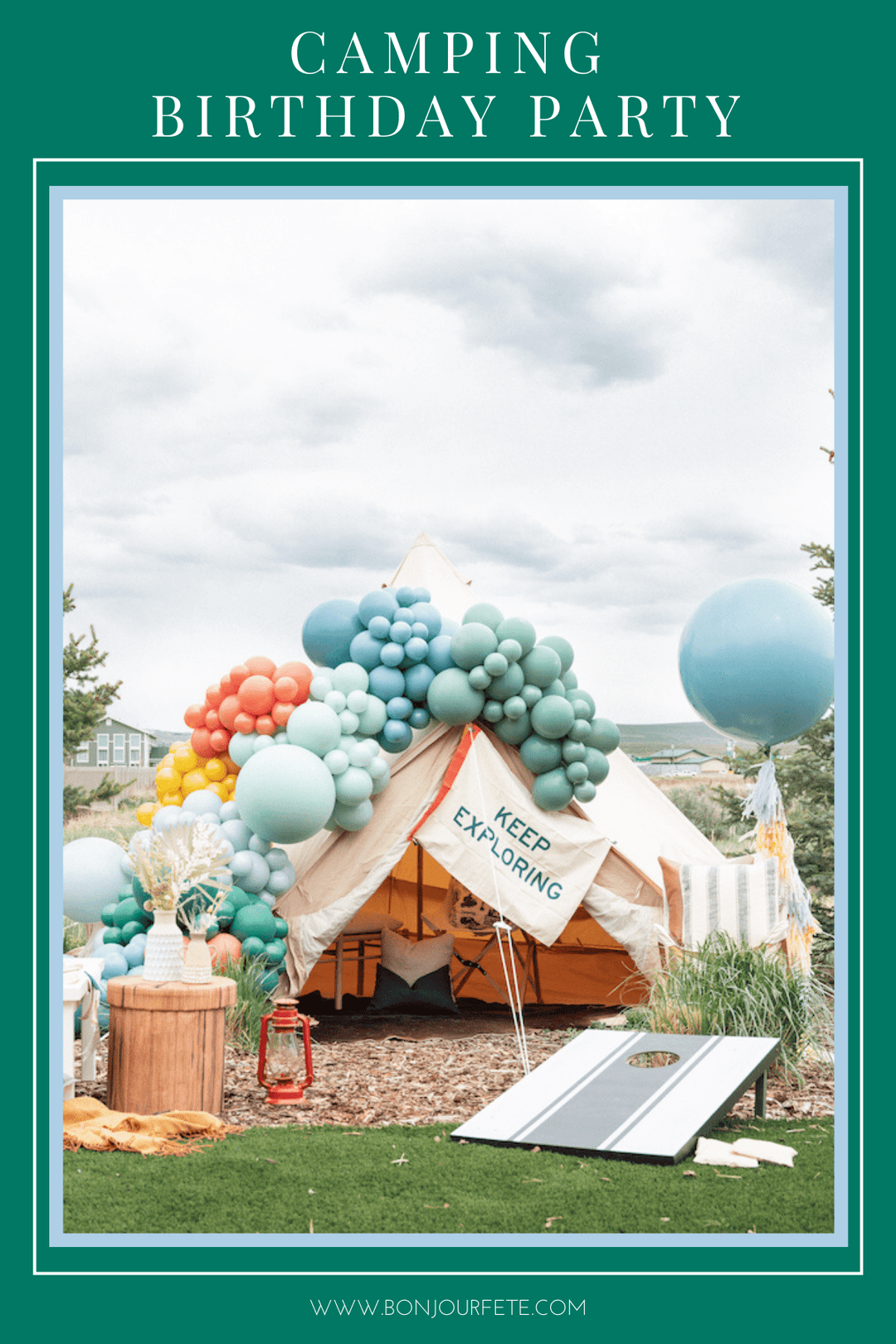 Outdoor camping birthday party with a canvas tent, blue and green balloon garland, cornhole game, and red lantern.