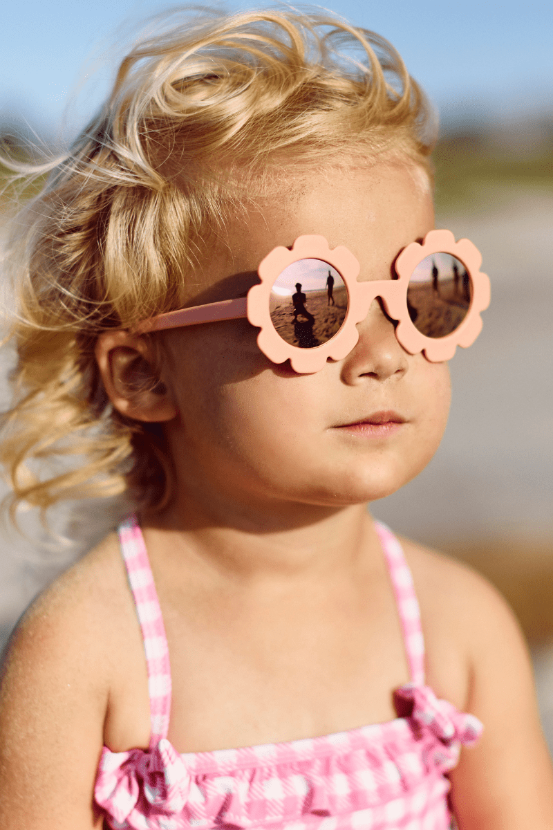Babiators kids sunglasses with flower-shaped peachy pink frames and rose gold mirrored UV lenses for babies and toddlers.