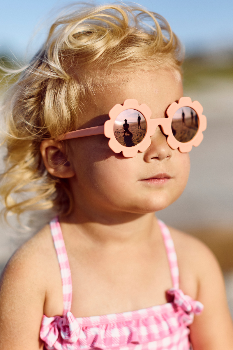 Babiators kids sunglasses with flower-shaped peachy pink frames and rose gold mirrored UV lenses for babies and toddlers.