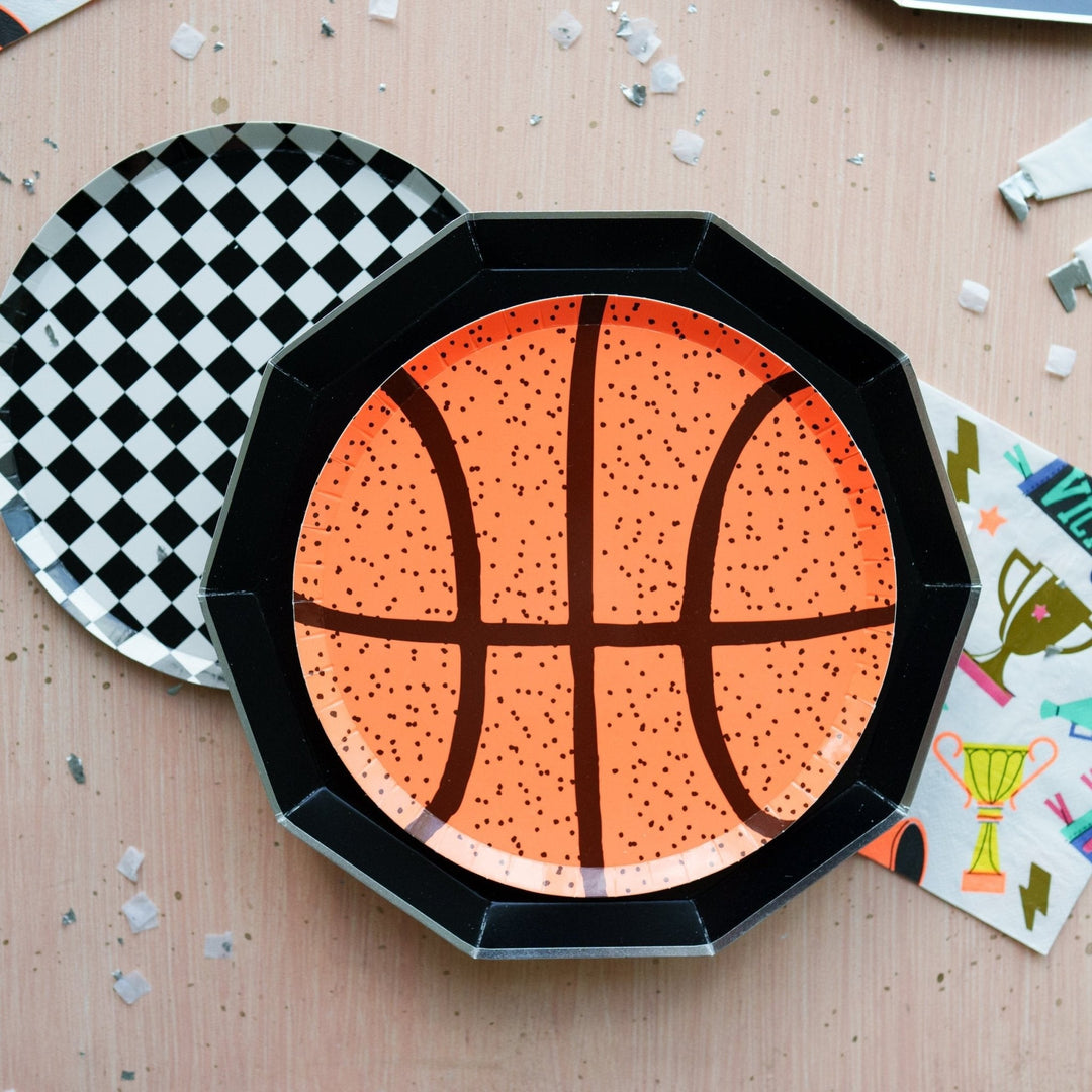 Black noir dinner plate layered under a basketball plate with a checkered plate and trophy napkin for a sports party