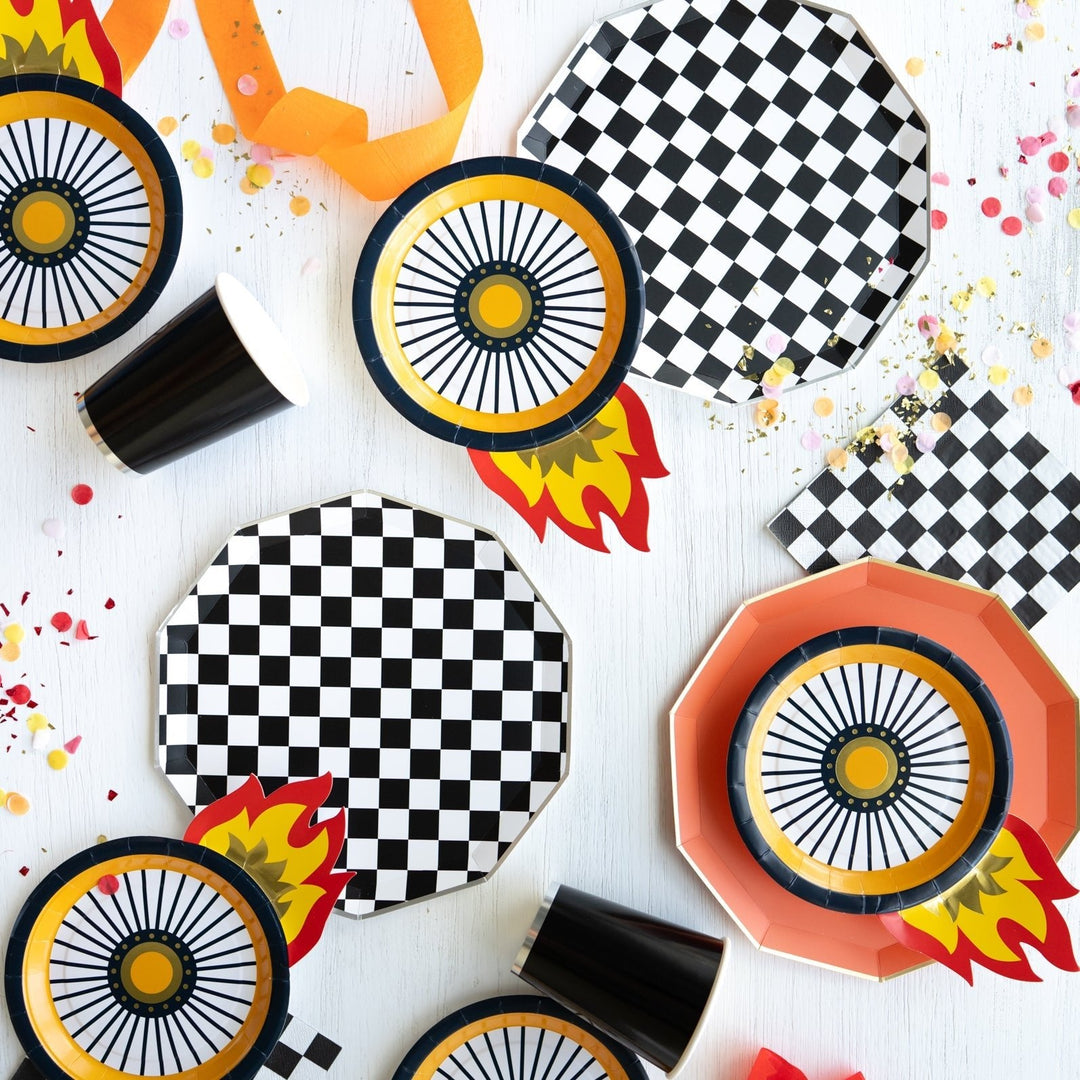 Race car party flat lay with checkered napkins, wheel print plates, flame decorations, and orange streamers