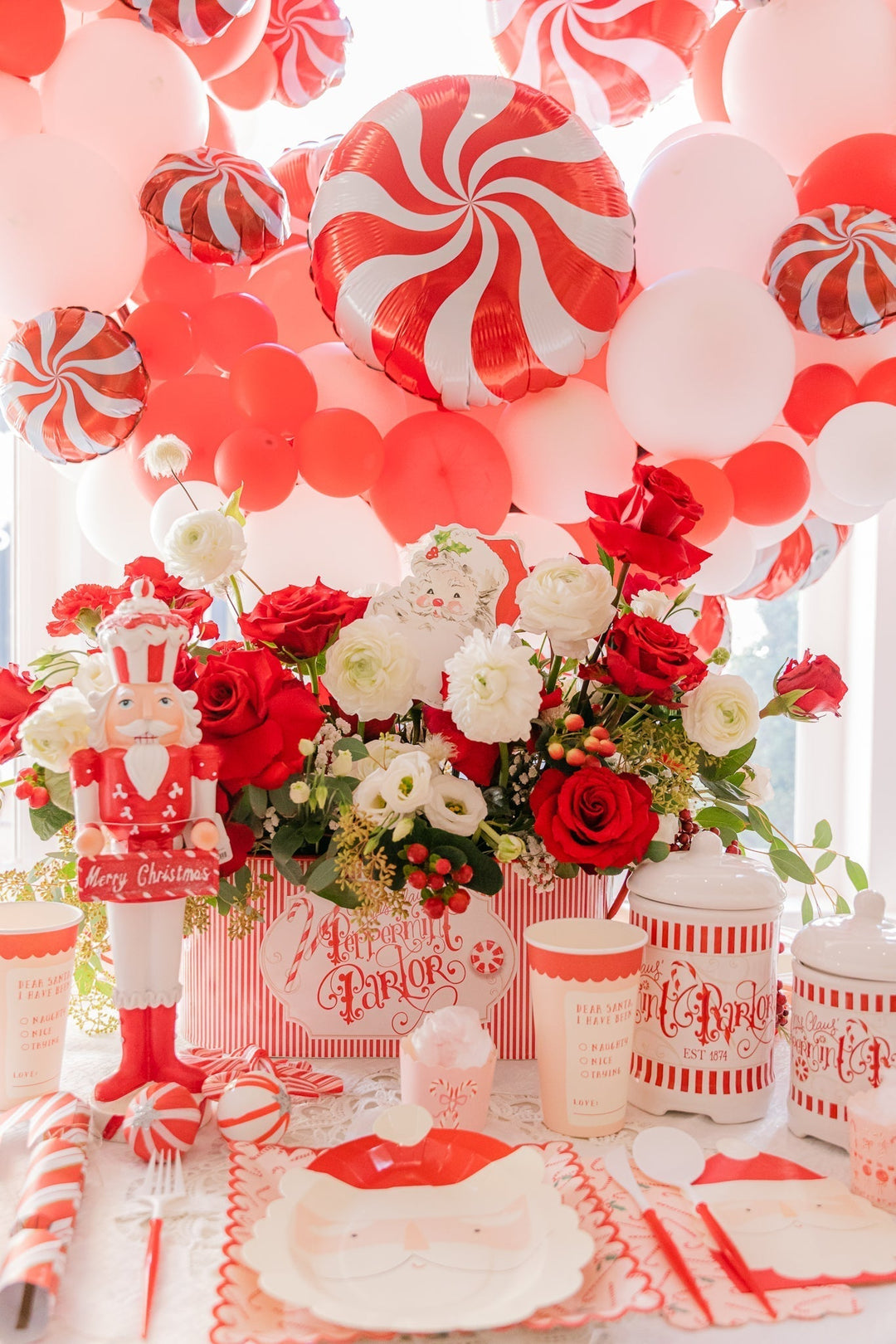 Red and white Christmas balloon garland with peppermint swirl foil balloons over a nutcracker and candy-themed holiday tablescape.