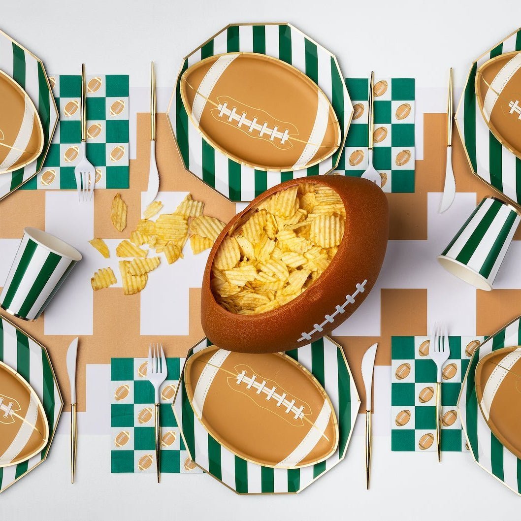 Football party table set with green stripe plates, football die-cut plates, checker napkins, and a football bowl of chips