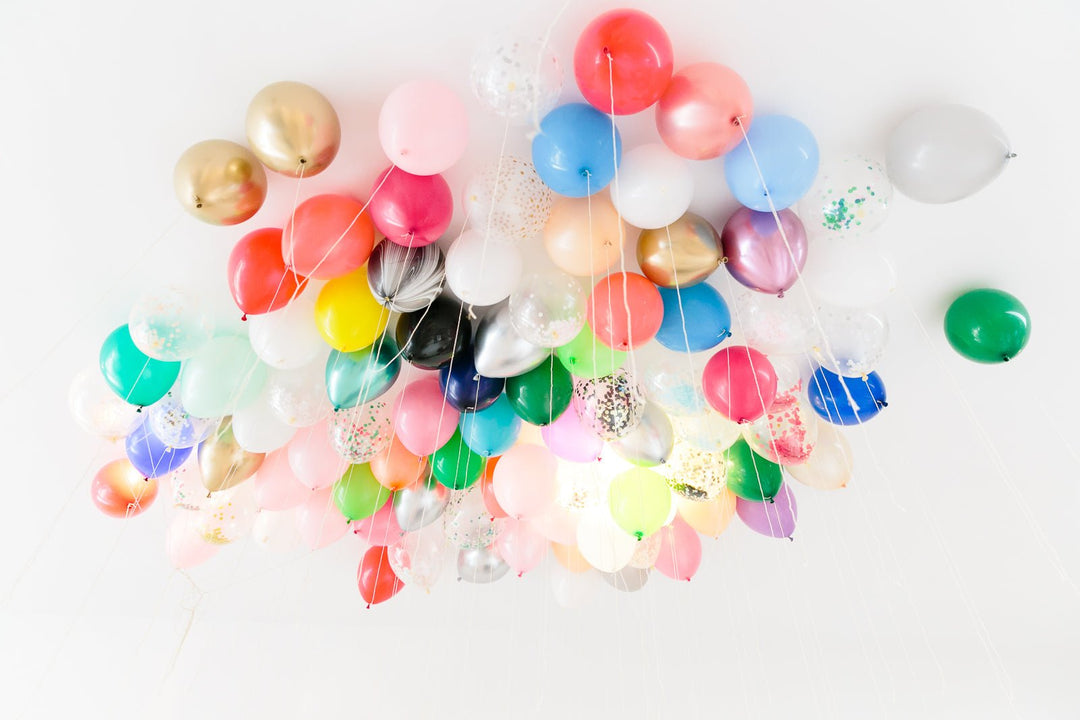 Colorful latex balloons in pink, gold, blue, green, and confetti designs floating on a white ceiling for a birthday party.