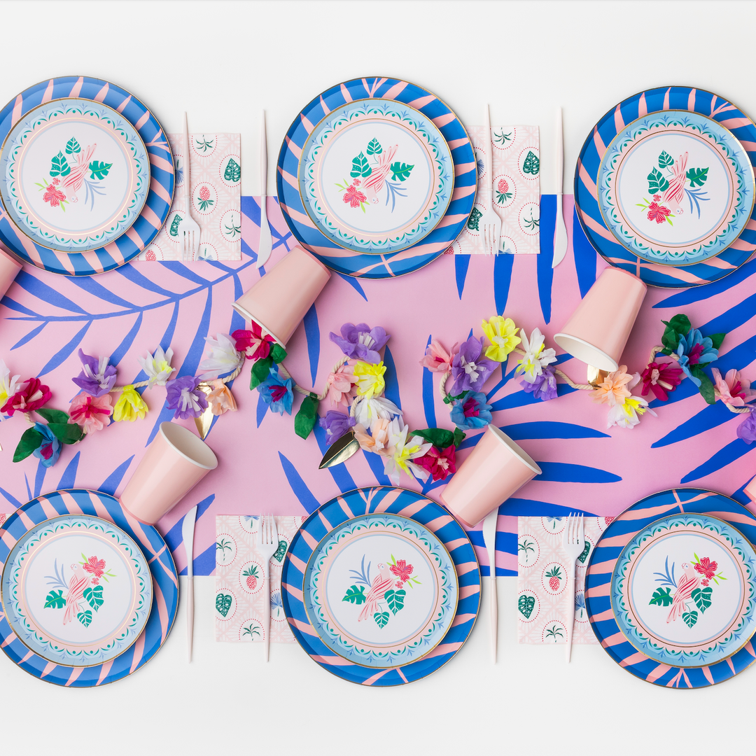 Pool party table with blue cabana stripe plates, tropical napkins, and a beach ball balloon for a summer birthday or luau.