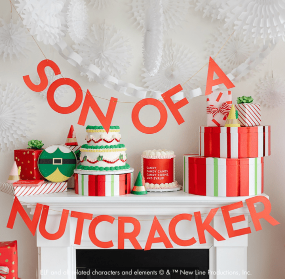 Close view of the Son of a Nutcracker banner above a mantel of frosted cakes, elf plates, and striped gift boxes