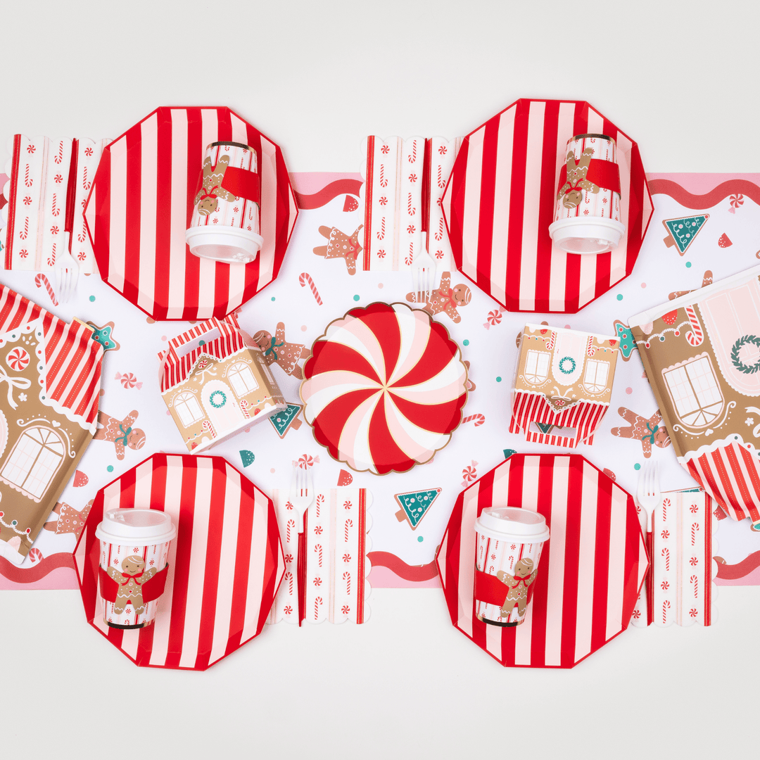 Christmas gingerbread party table with red striped plates, a peppermint swirl plate, and gingerbread house favors