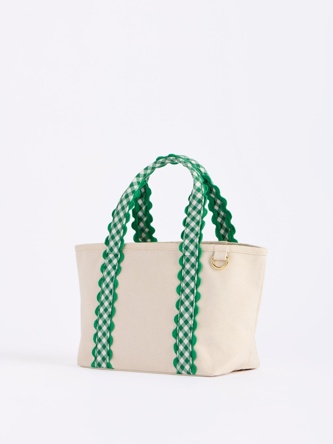 A cream canvas tote bag with green and white gingham patterned handles and a small gold metal ring detail, photographed on a clean white background.