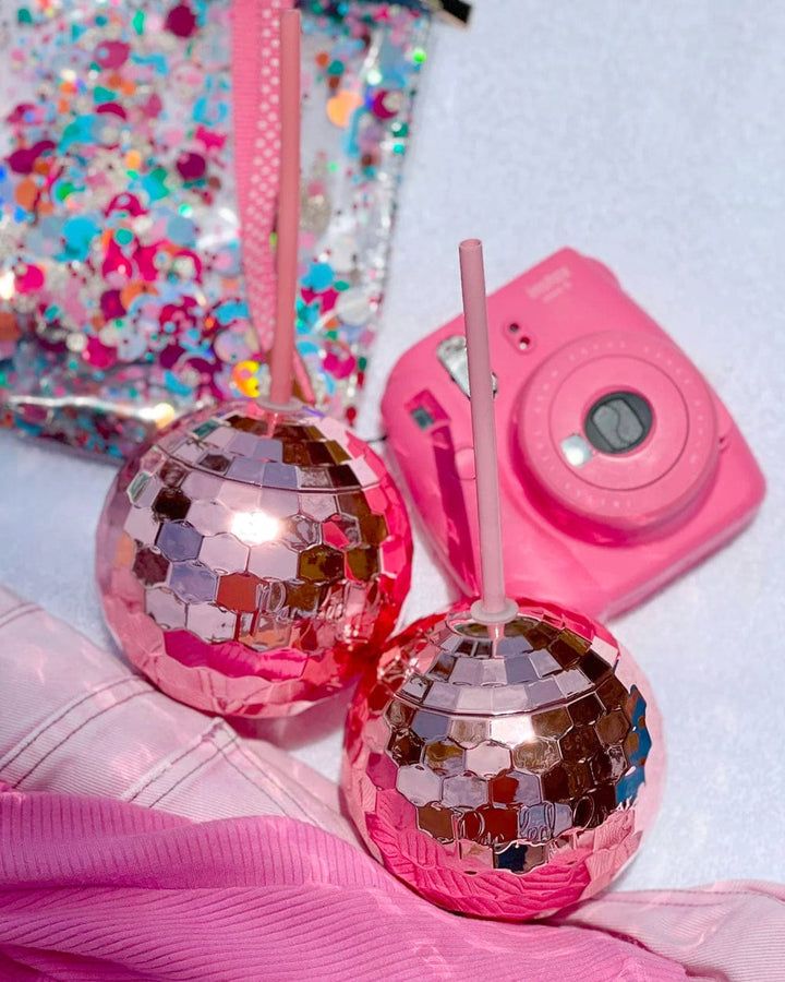 Two pink disco ball cups next to a pink instant camera and a sequin confetti pouch