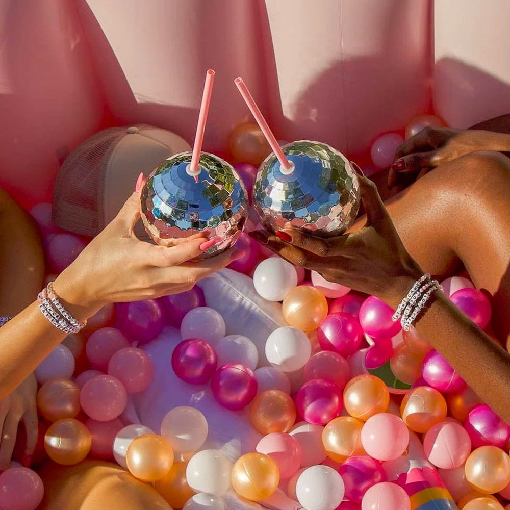 Two friends in a pink ball pit toasting with silver disco ball cups