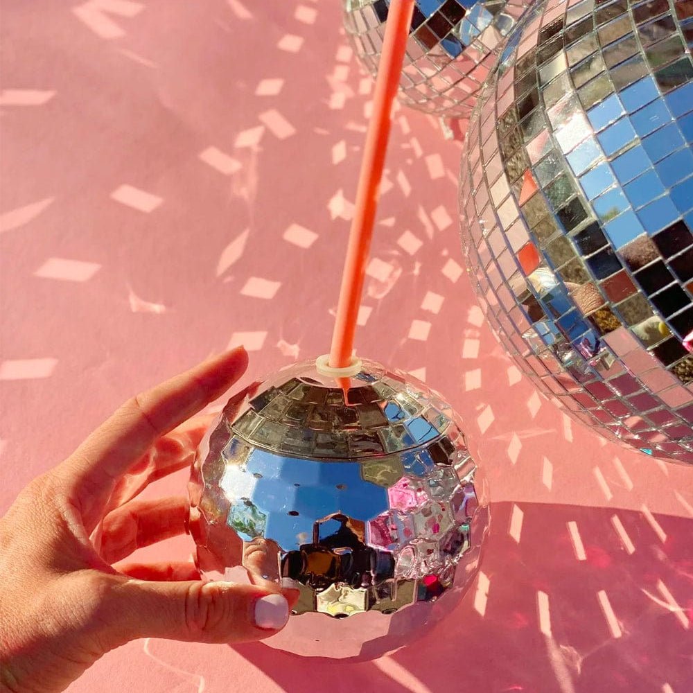 Hand holding a silver disco ball cup under a large mirror ball on a pink backdrop