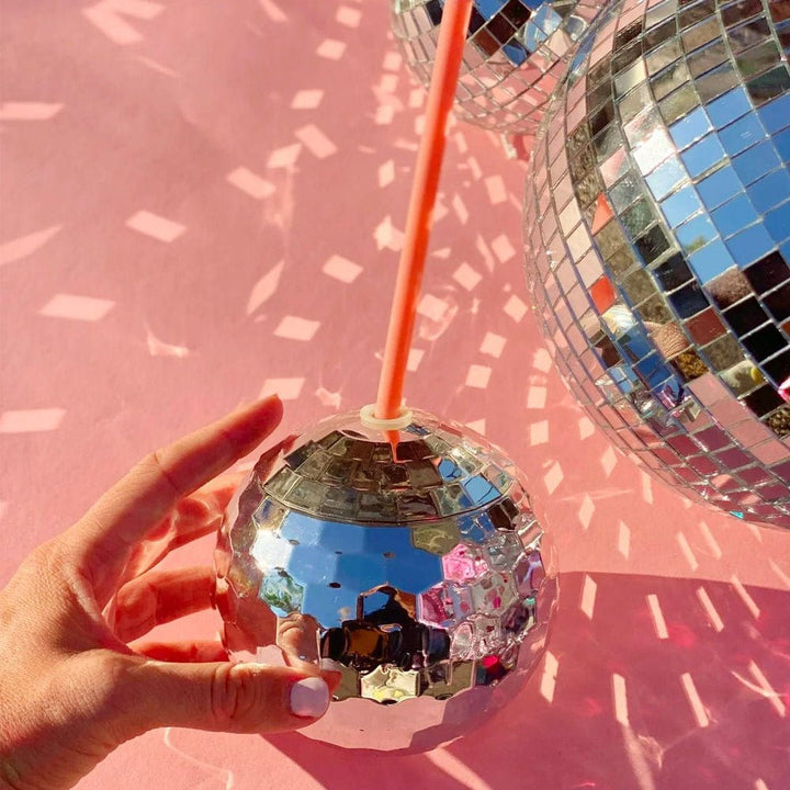 Hand holding a silver disco ball cup under a large mirror ball on a pink backdrop