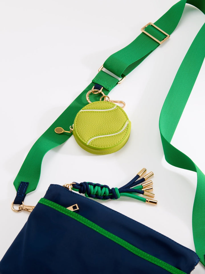 A tennis-themed crossbody bag featuring a bright green webbed strap, a navy blue body, a green zipper trim, a tennis ball-shaped charm, and a green and navy tassel detail, shown on a clean white background.