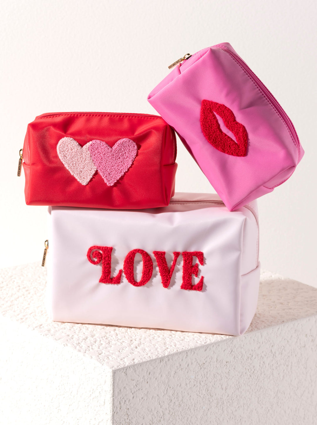 Blush LOVE pouch under a red heart pouch and a pink lips pouch on stone, styled for Galentine's