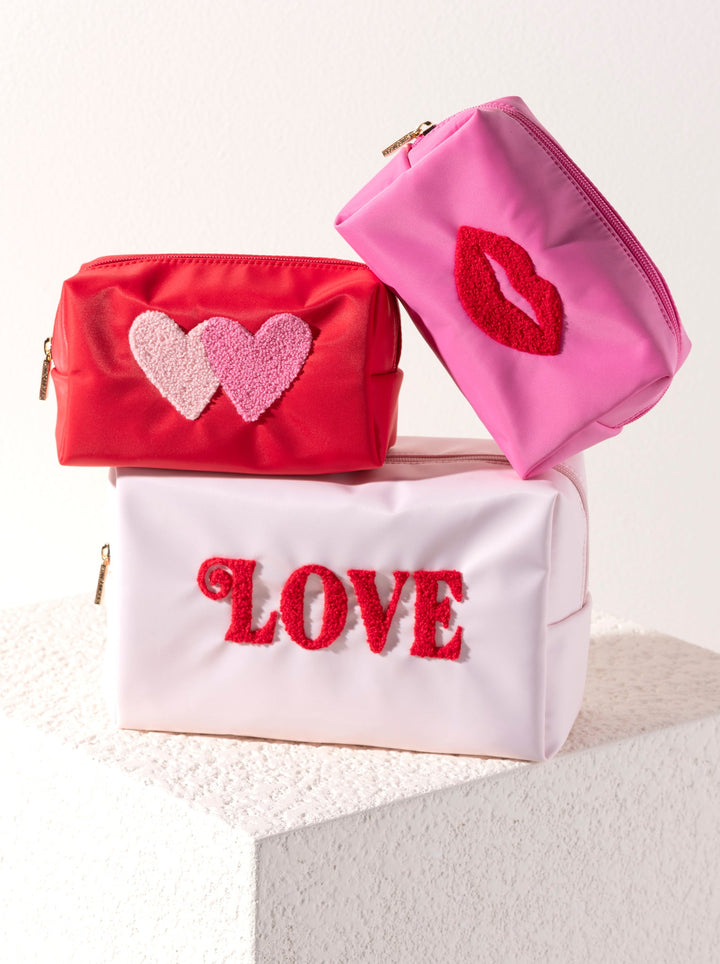 Blush LOVE pouch under a red heart pouch and a pink lips pouch on stone, styled for Galentine's