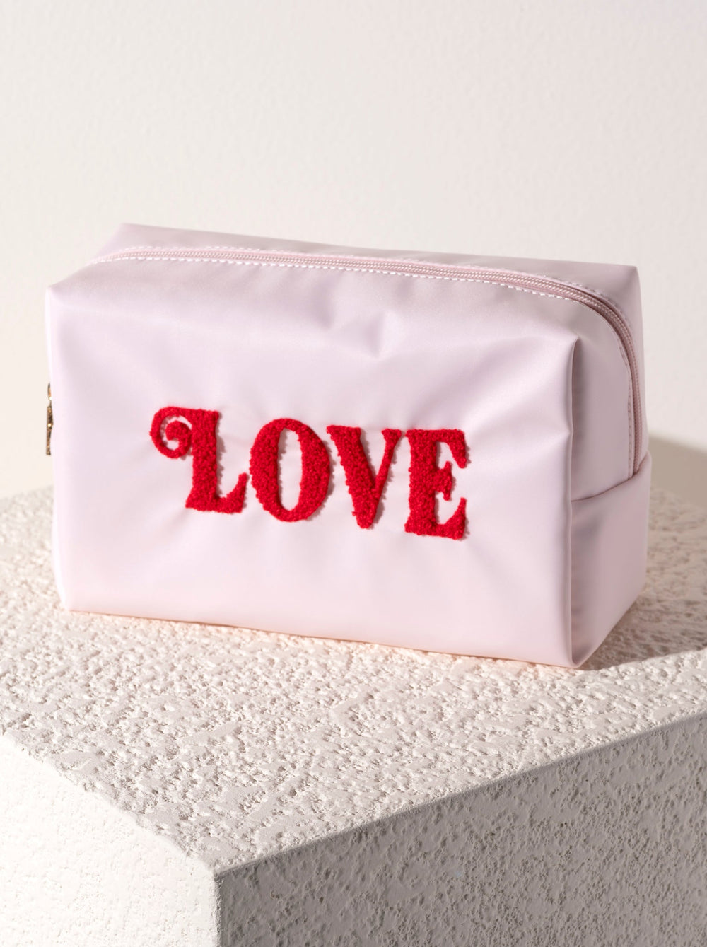 Blush LOVE makeup bag standing on a white stone block, a sweet Valentine's Day gift for her