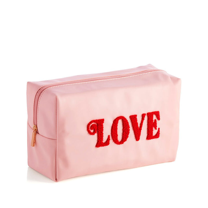 Blush pink LOVE cosmetic pouch with raised red sherpa letters and a gold zipper, angled on white