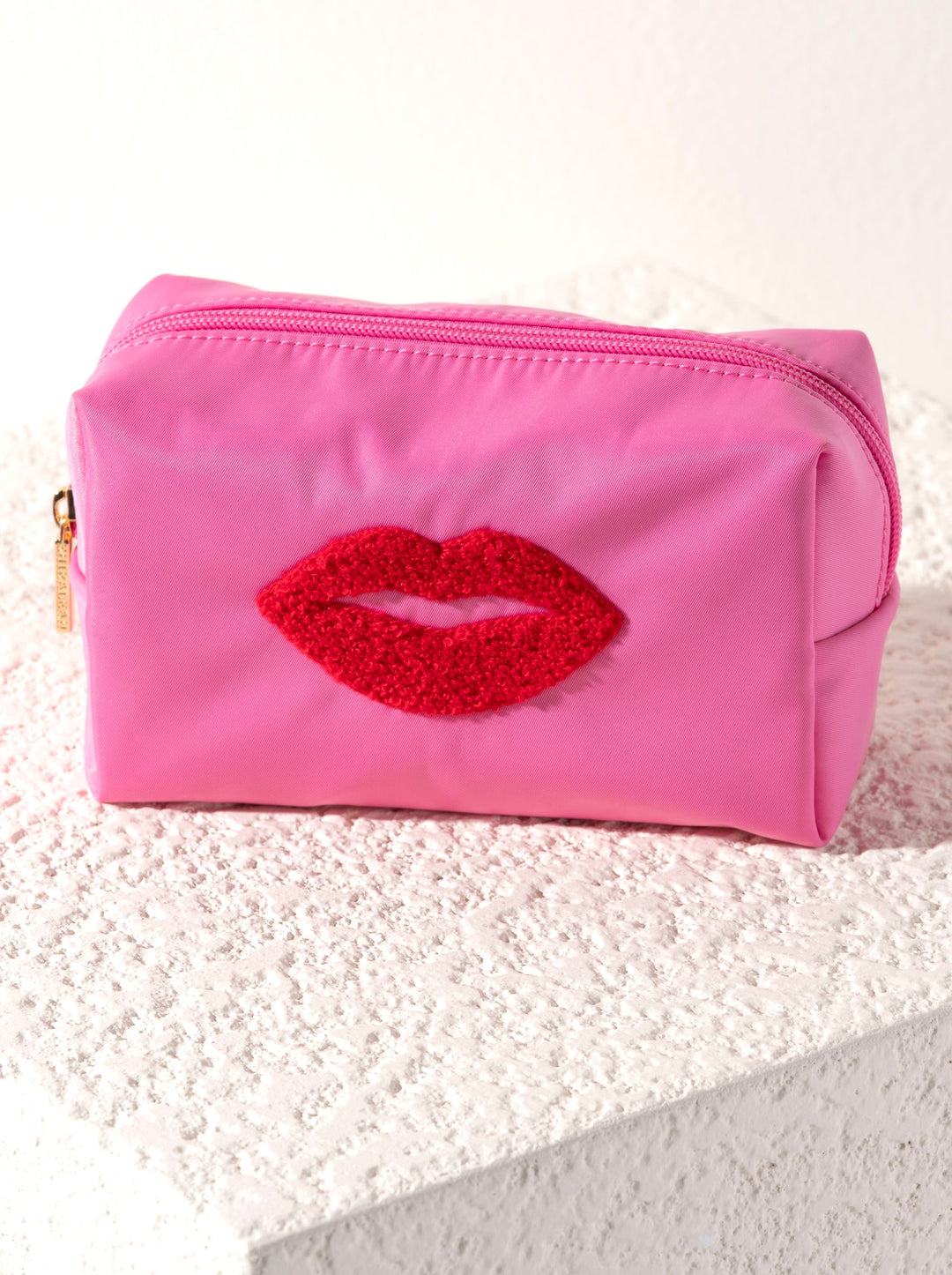 Pink pouch with red lip design on a textured surface