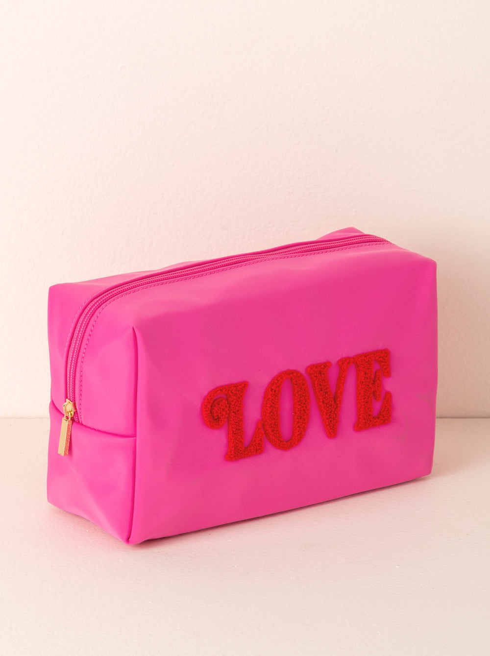 Pink LOVE cosmetic pouch with a gold zipper styled on a blush backdrop