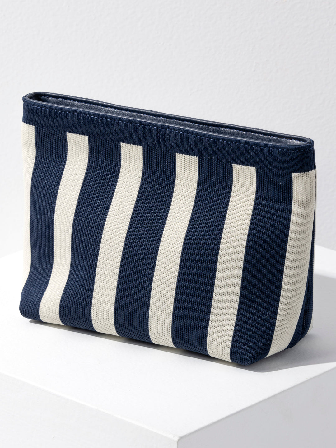 A zippered pouch with vertical navy blue and off-white stripes, shown on a white pedestal against a light gray background.