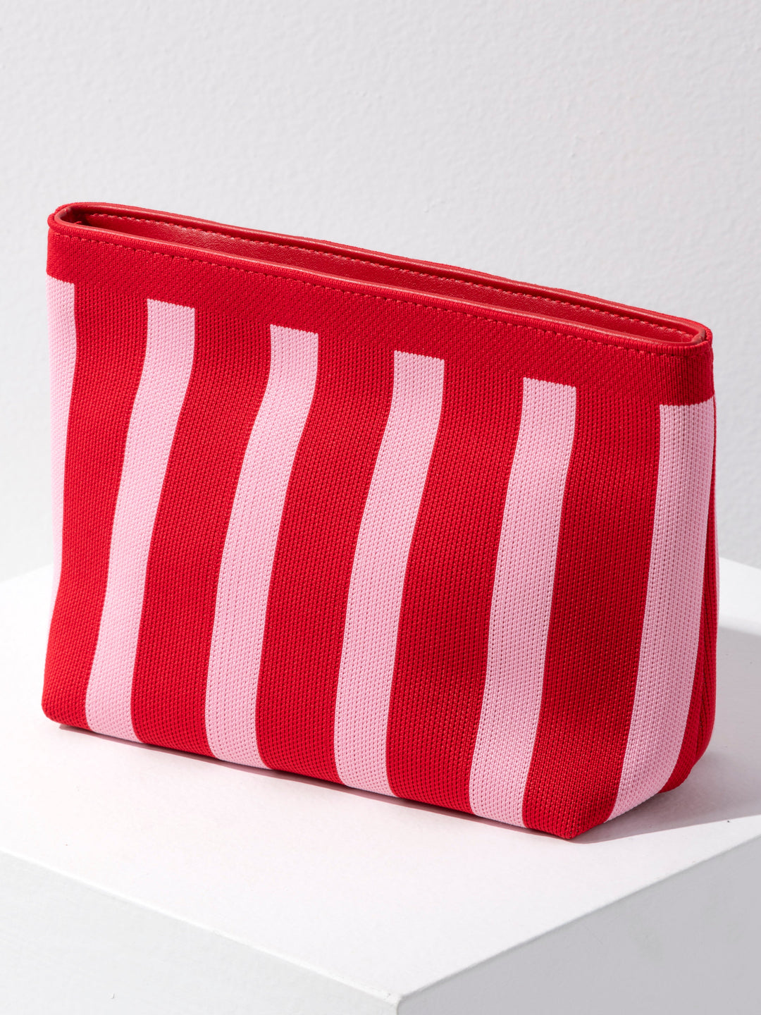 A red and light pink vertically striped canvas pouch with a zip-top closure, displayed on a white surface against a light gray wall.