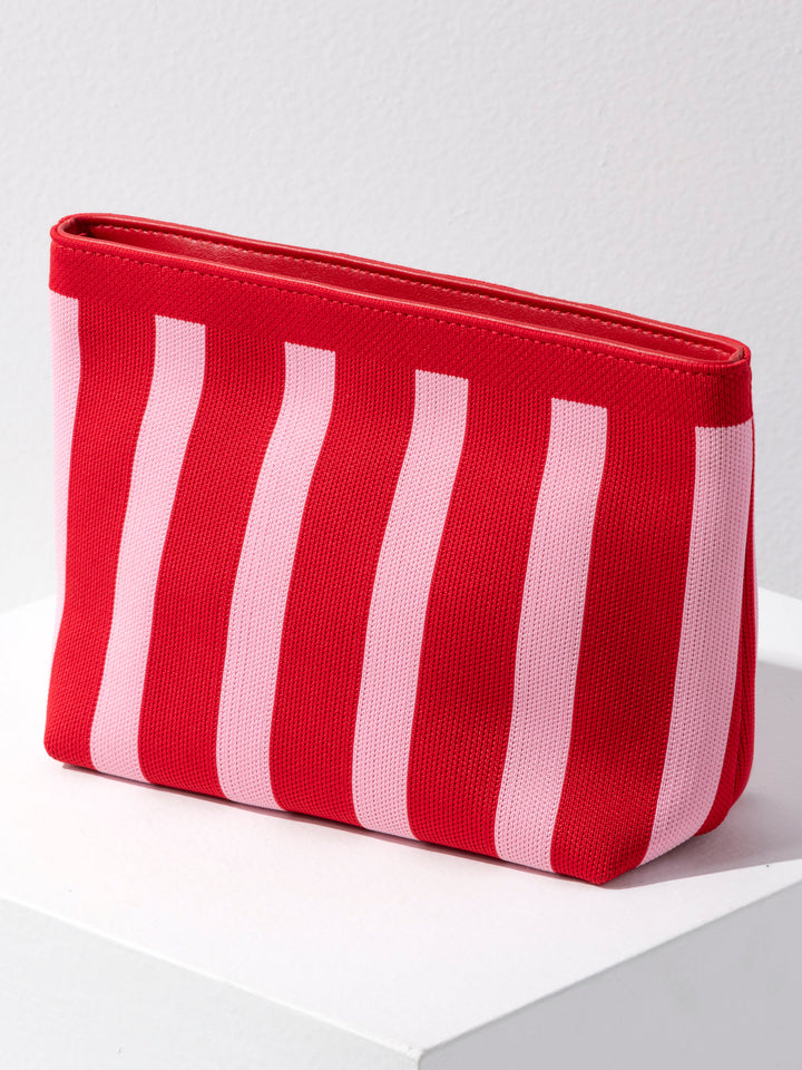 A red and light pink vertically striped canvas pouch with a zip-top closure, displayed on a white surface against a light gray wall.