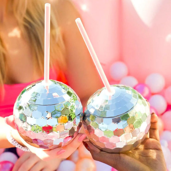 Two hands clinking silver disco ball cups over a pink and white balloon pit