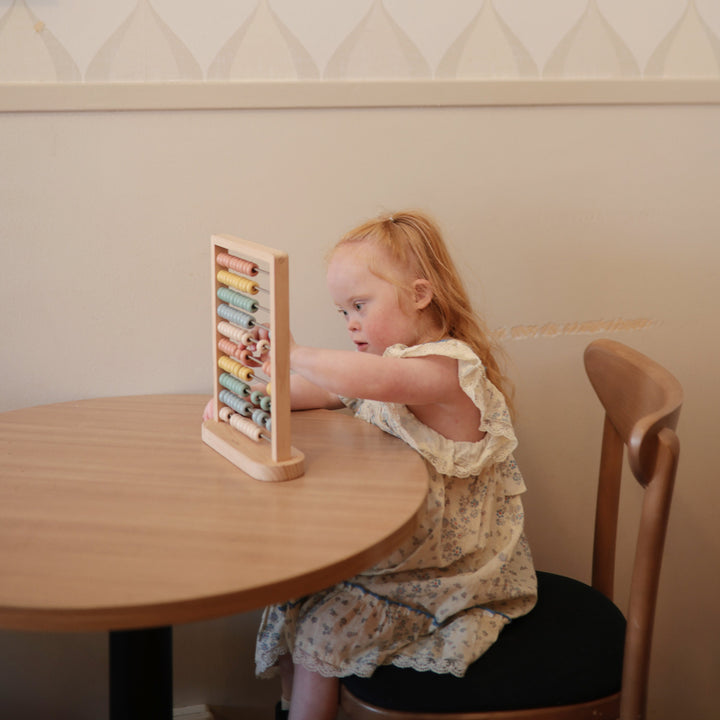 Toddler counting beads on the Mushie wooden abacus