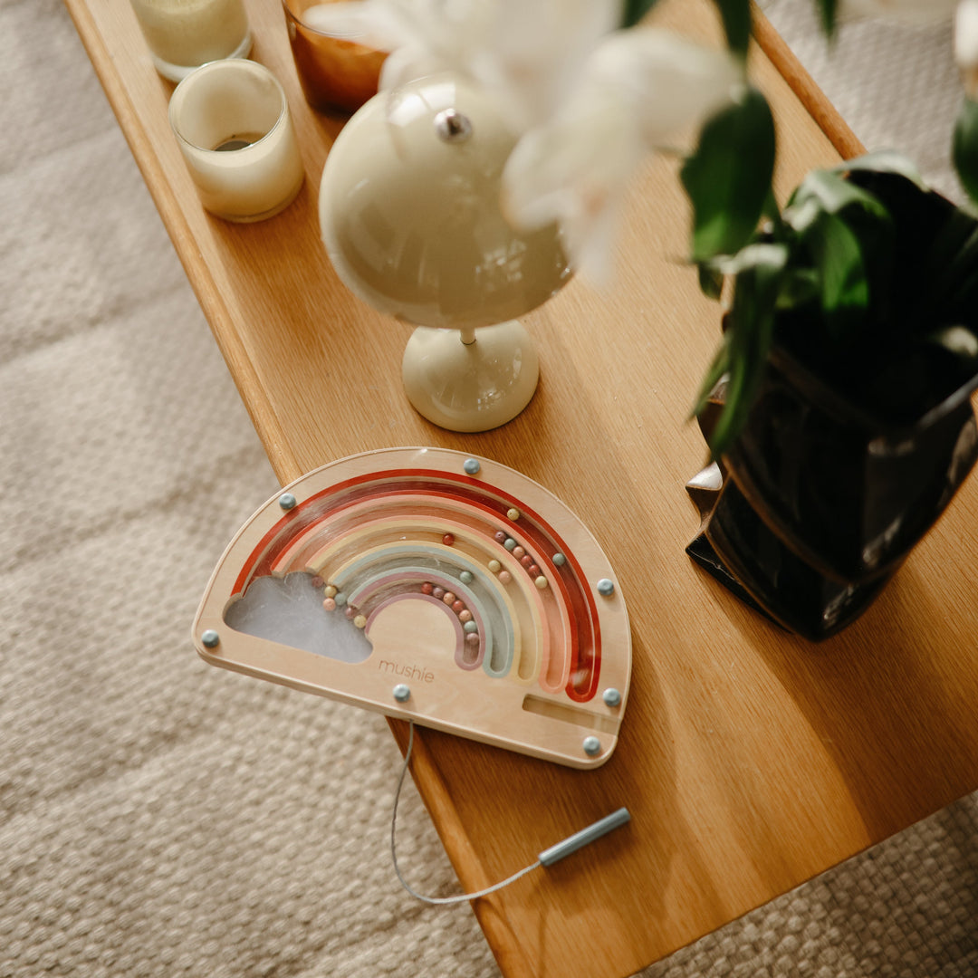 Toddler playing with the Mushie wooden magnetic rainbow maze