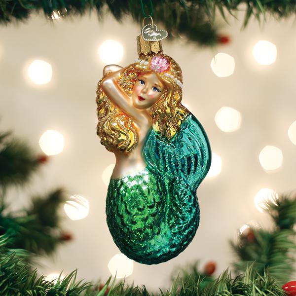 Seashell mermaid ornament hanging on a lit Christmas tree with soft bokeh lights