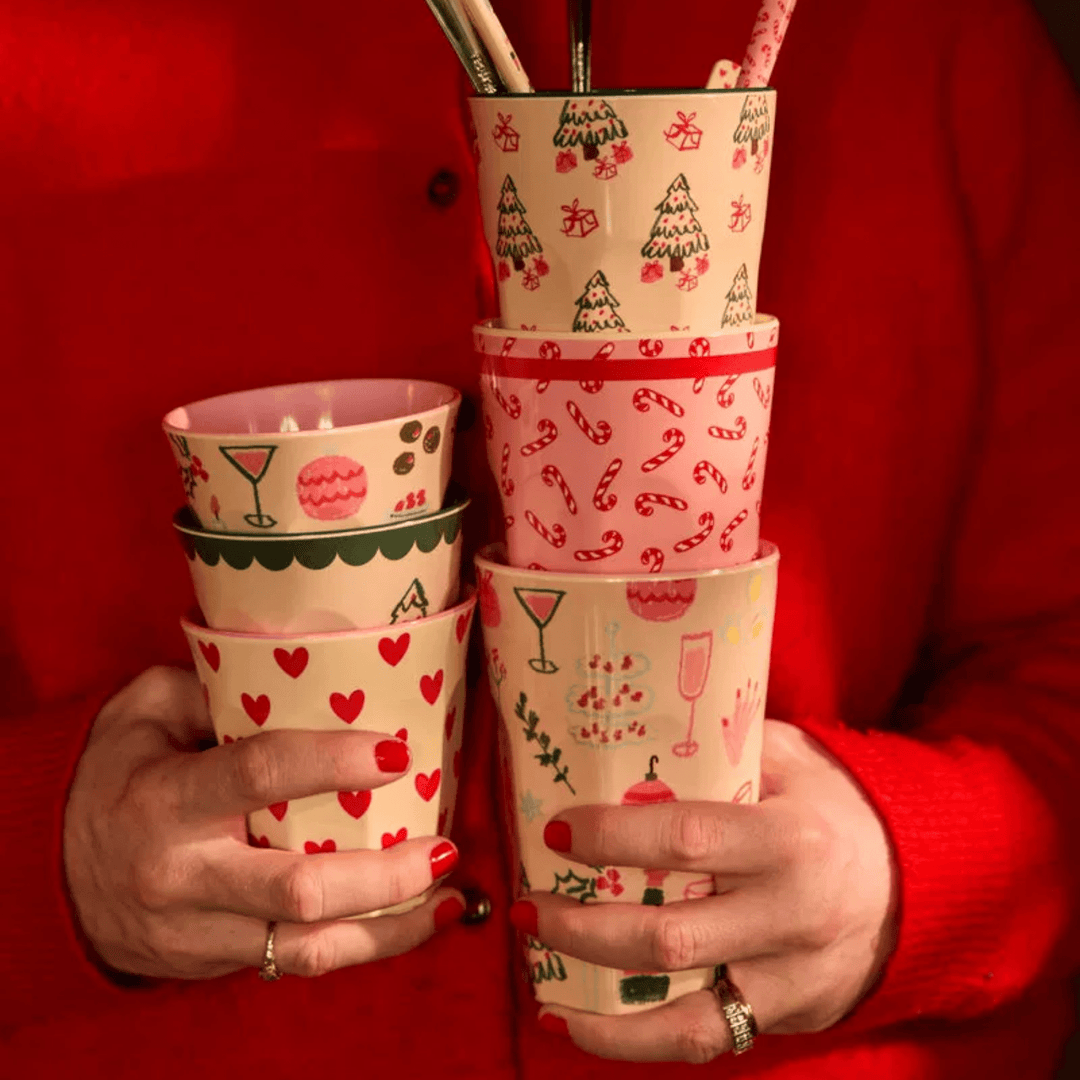 Hands holding a stack of Rice melamine Christmas cups in candy cane, tree, heart, and cocktail prints