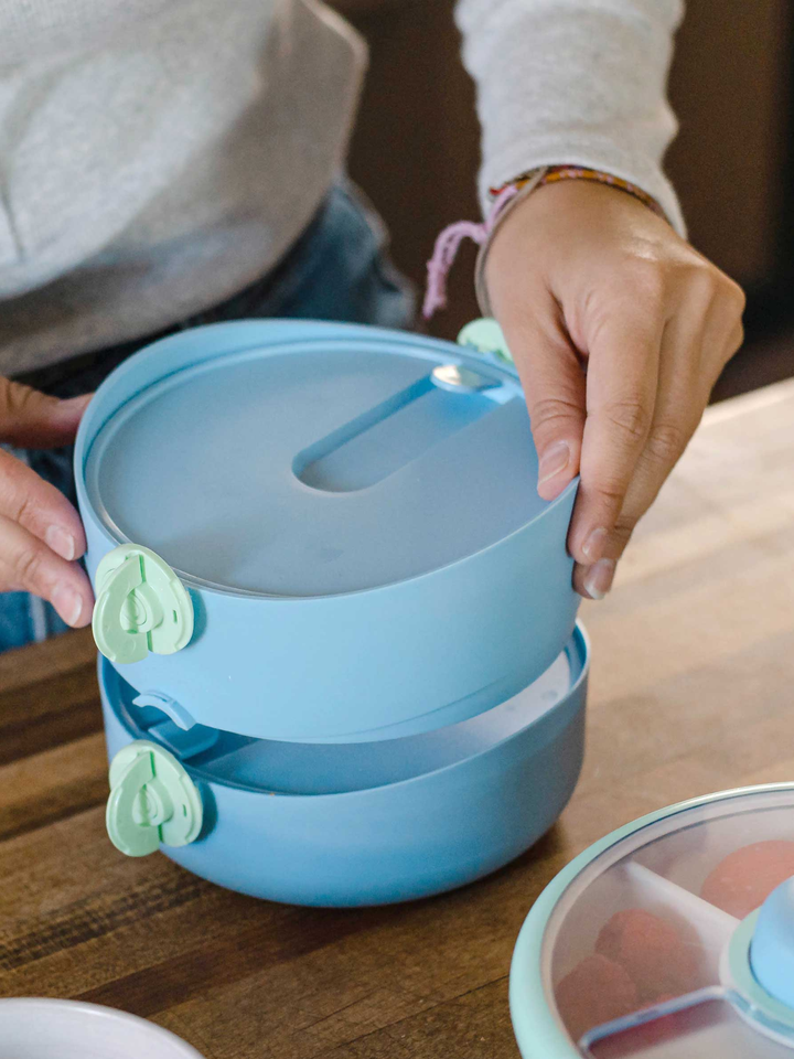Adult stacking the blue Lunch Stack compartments together on a kitchen counter
