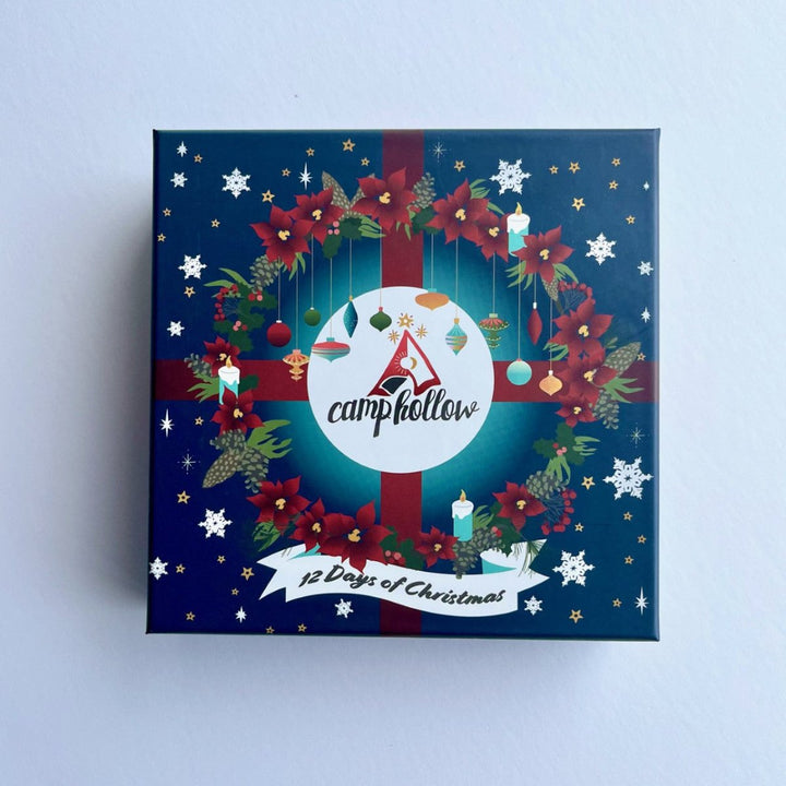 A square Christmas advent box by CampHollow, featuring a dark blue background decorated with a red and green wreath, red poinsettias, white snowflakes, and a white circular logo in the center.