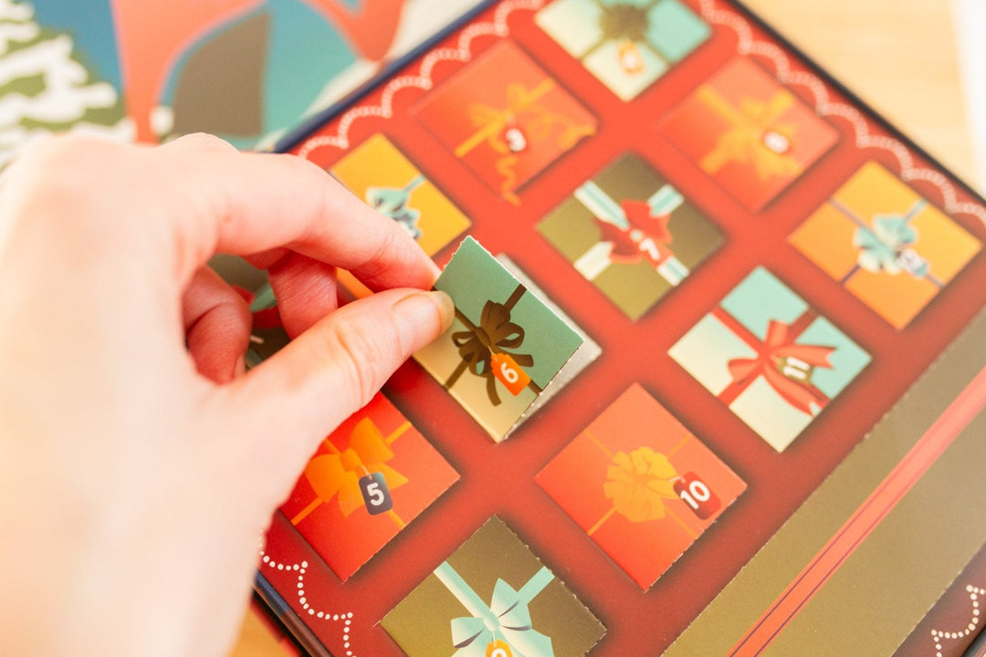 A close-up of a hand sliding an advent card from a colorful Christmas advent calendar box.