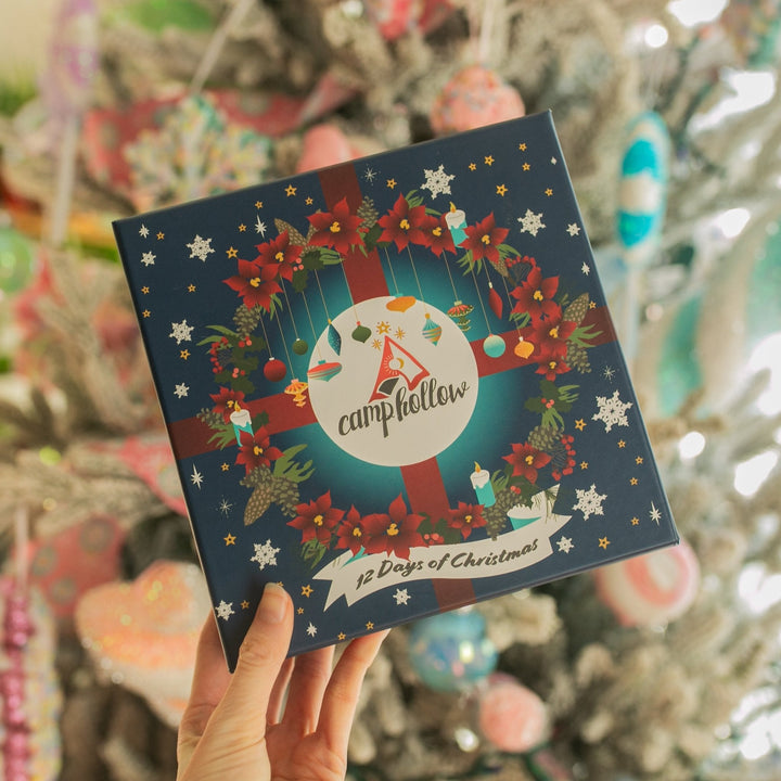 Hand holding the 12 Days of Christmas advent box with a wreath, red ribbon, and snowflakes