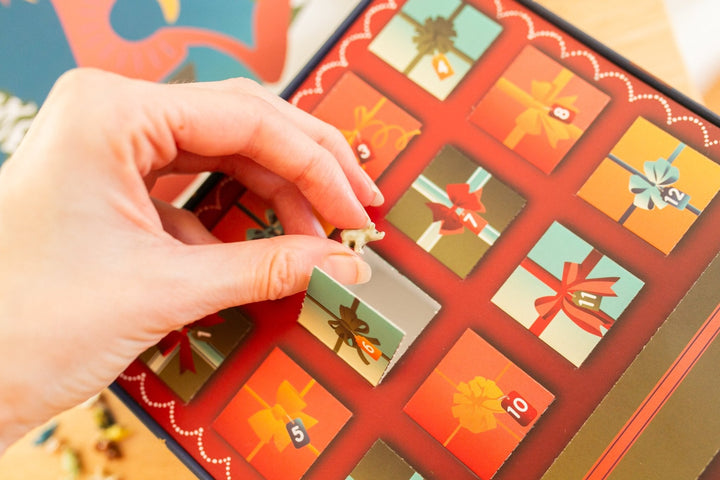 A close-up of a hand opening one of the numbered advent doors on a colorful gift-box themed advent calendar.