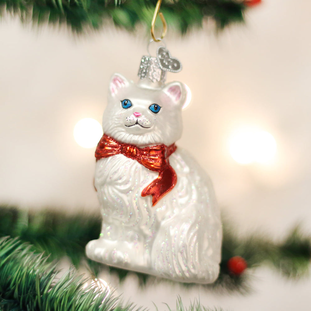 White cat ornament with a red bow hanging on a Christmas tree with glowing lights behind
