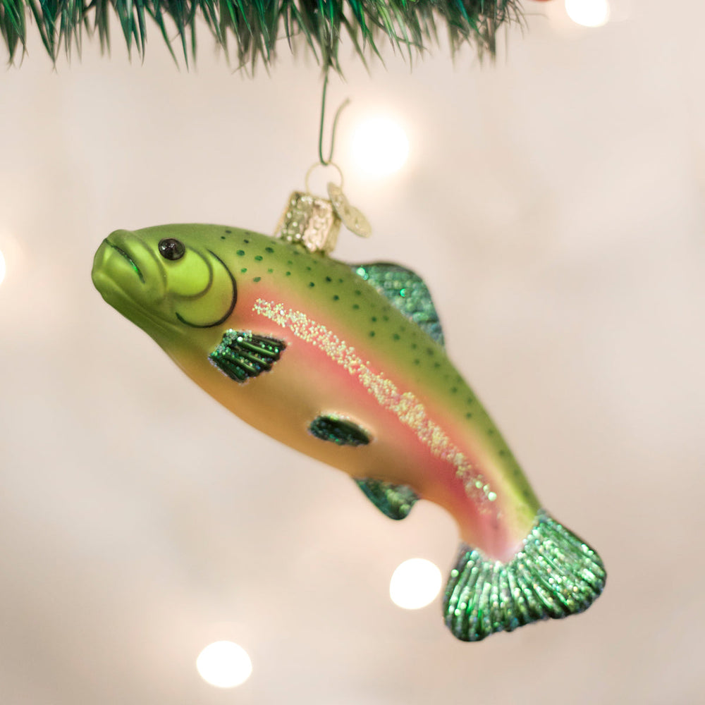 Rainbow trout ornament hanging from a pine branch against warm twinkle lights, a fishing gift for the tree