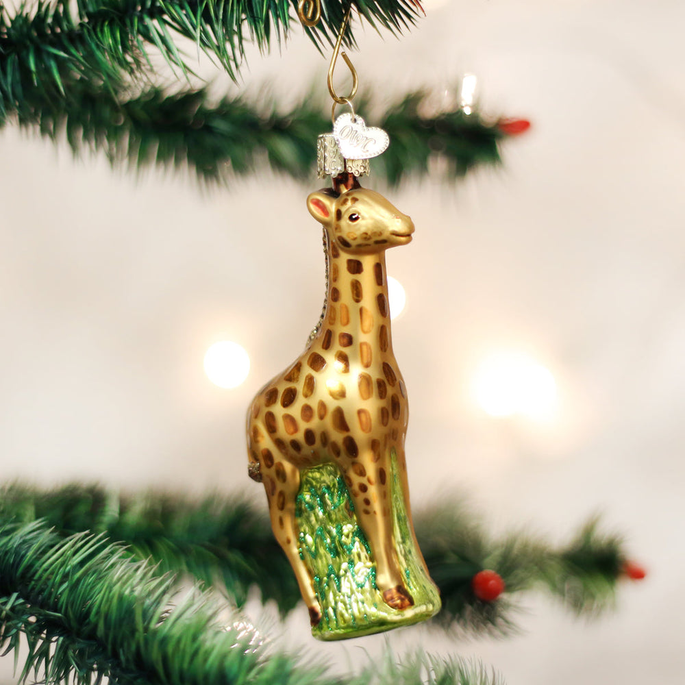 Spotted baby giraffe glass ornament standing on green grass, hanging on a Christmas tree