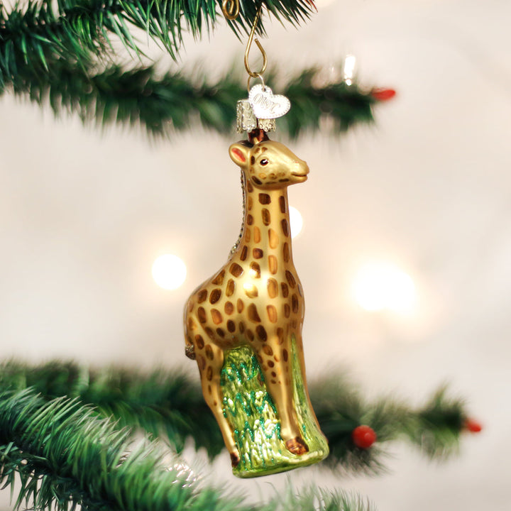 Spotted baby giraffe glass ornament standing on green grass, hanging on a Christmas tree