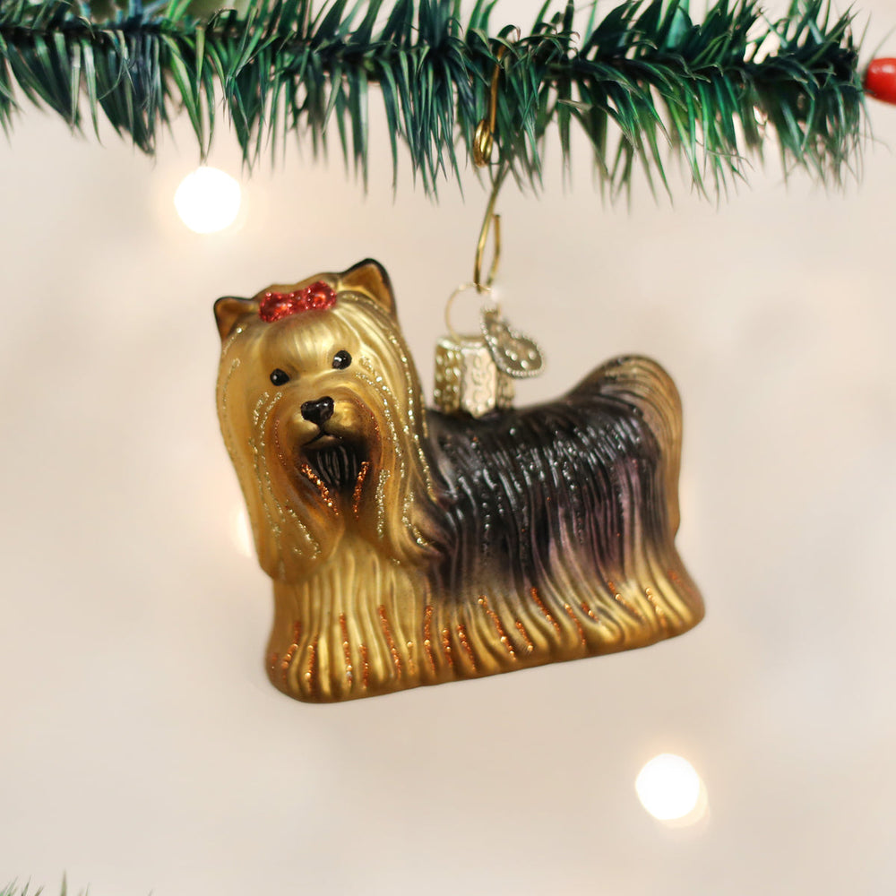 Yorkie glass ornament hanging under pine garland on a twinkling Christmas tree