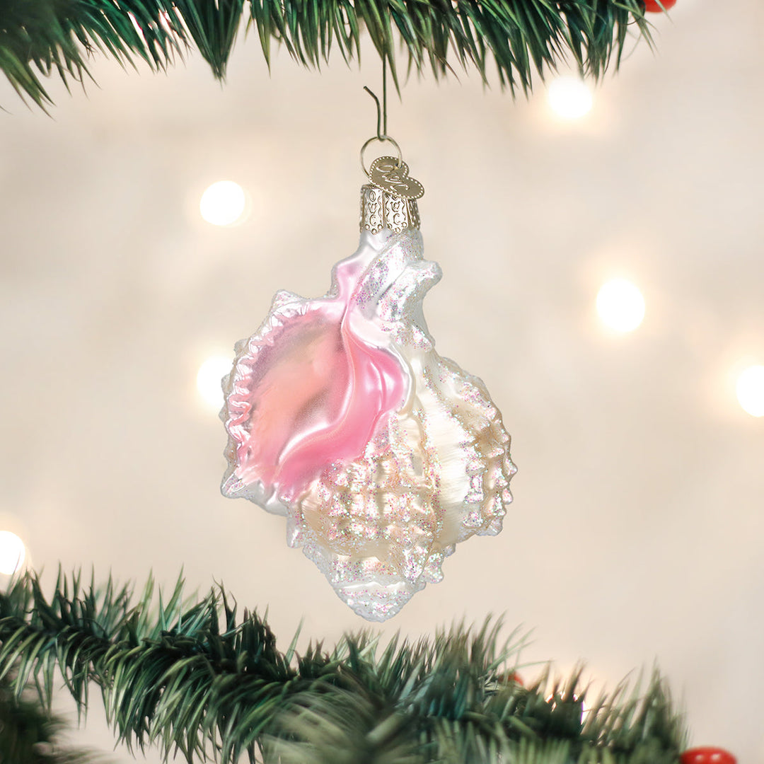 Pink Mexican shell ornament hanging on a lit Christmas tree with warm bokeh lights