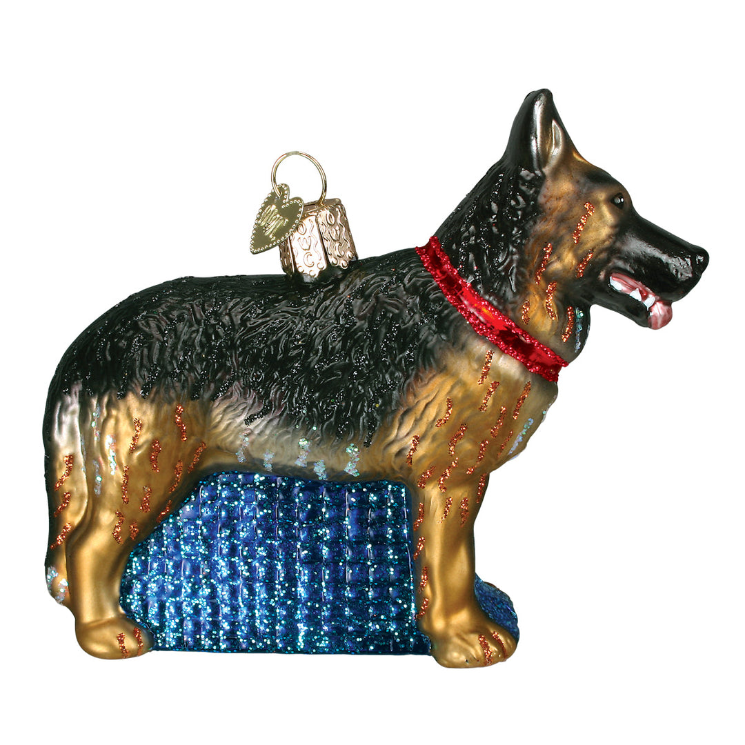 Black and tan German Shepherd ornament in a red collar on a blue glitter base, side view