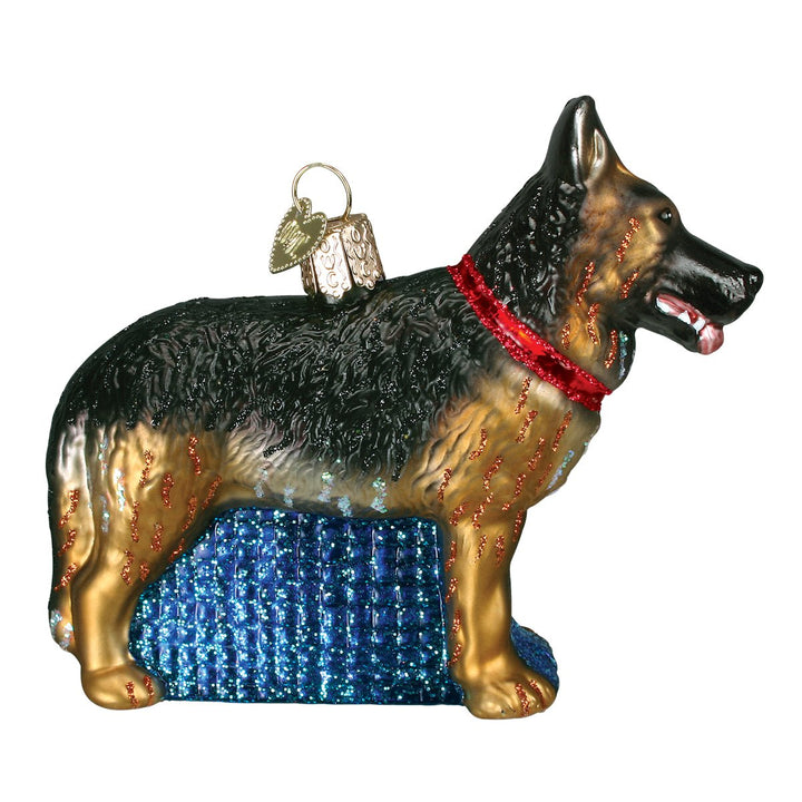Black and tan German Shepherd ornament in a red collar on a blue glitter base, side view