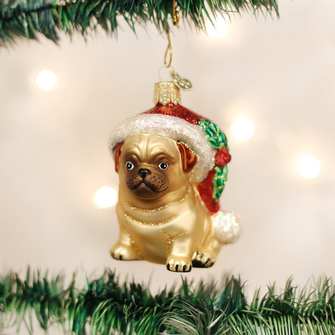 Holly hat pug glass ornament hanging on a Christmas tree with warm bokeh lights