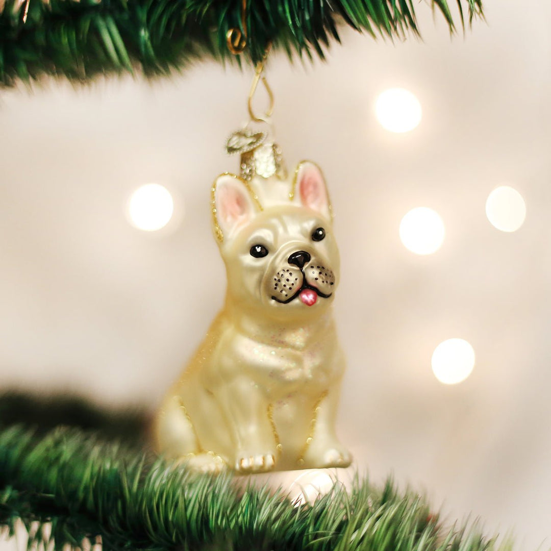 Cream French bulldog glass ornament sitting upright with pink ears, hanging on a Christmas tree