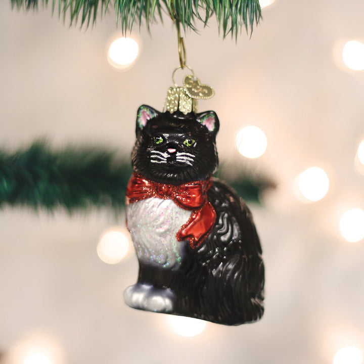 Tuxedo cat ornament with red bow hanging on a Christmas tree against soft holiday lights