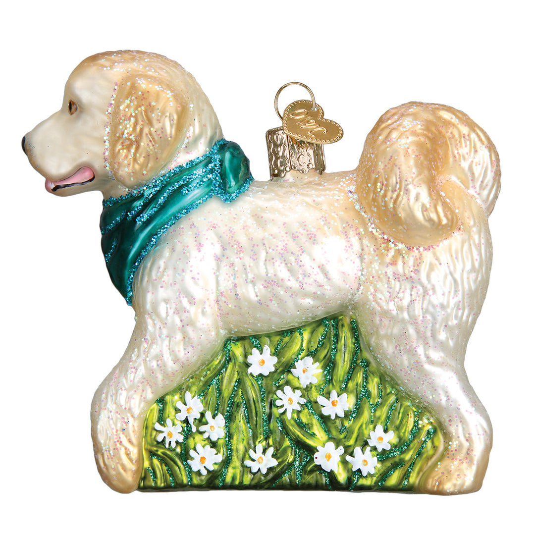 Cream doodle dog ornament in a teal bandana standing on green grass with white daisies, side view