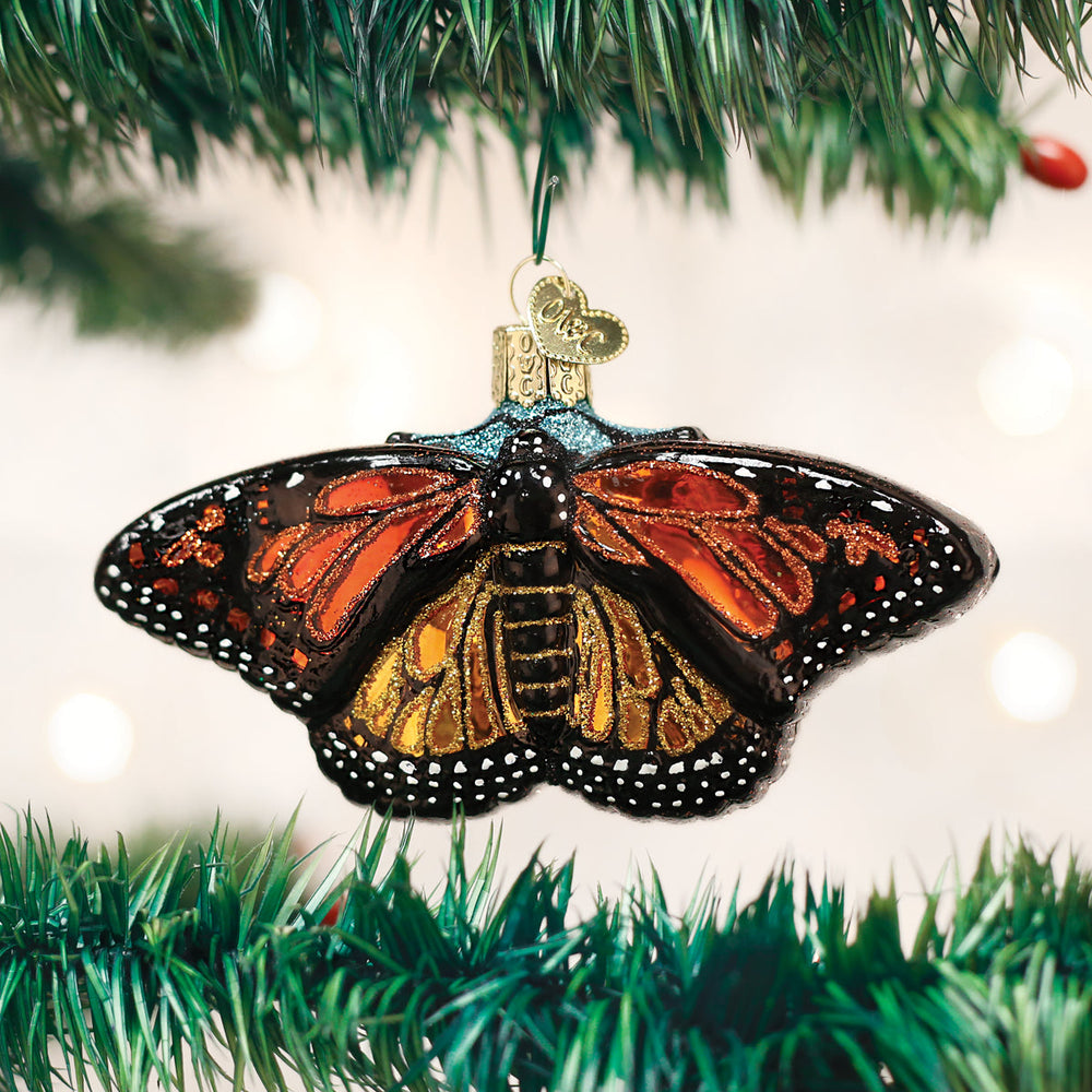 Monarch butterfly ornament with wings spread on a Christmas tree branch, holiday lights behind